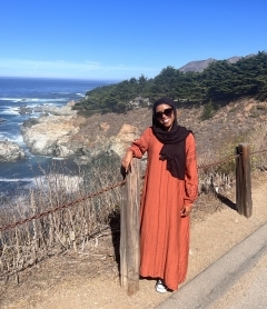 Student wearing an orange dress smiling in front of the California Coast