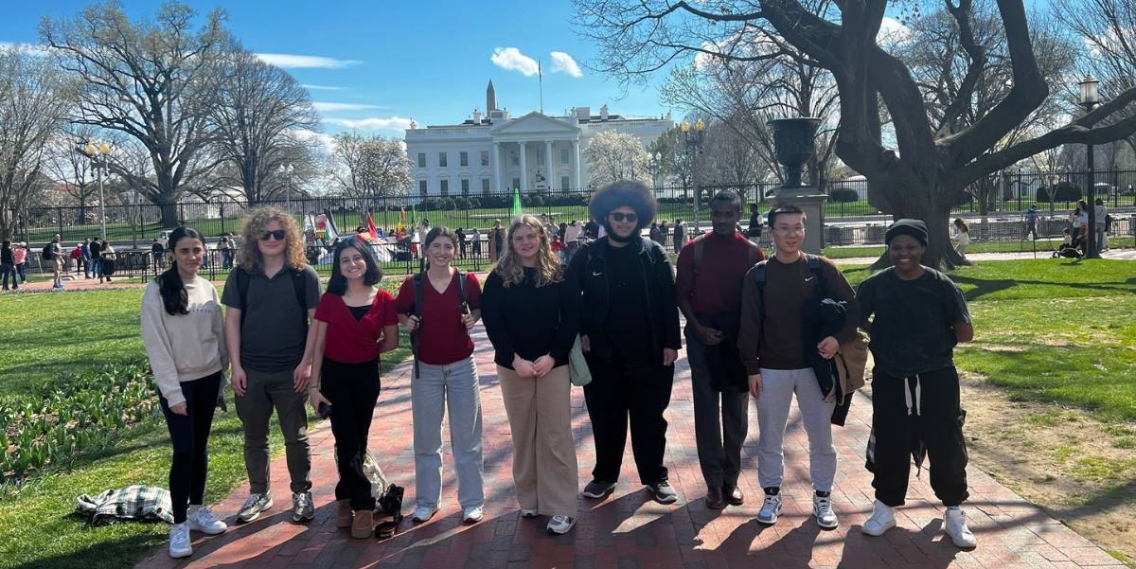 A group of students in casual clothes stand smiling in front of the White House.