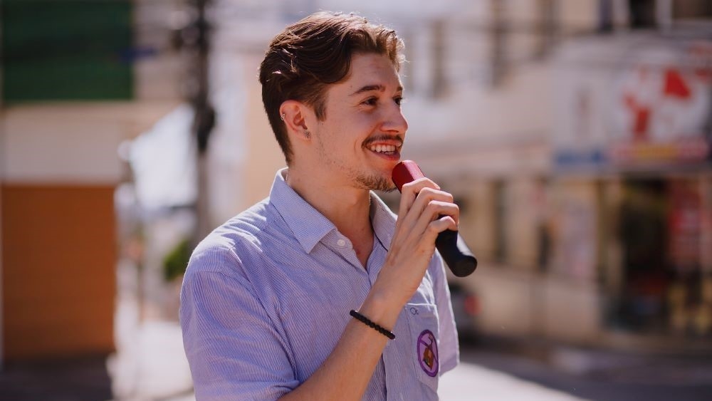 Arthur Martins speaks into microphone at outdoor Pride March.