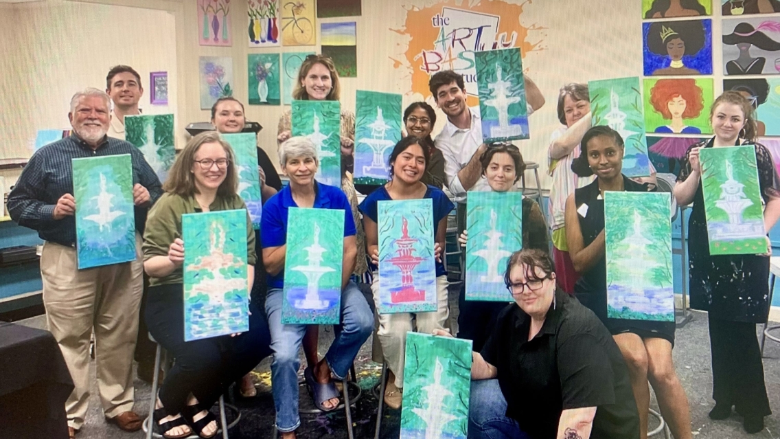 Group of people in a painting class showing their artwork to the camera.