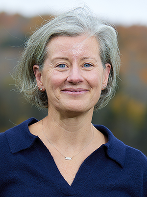 headshot of Janine Hetherington outside at Bread Loaf in autumn, wearing a navy knit collared shirt