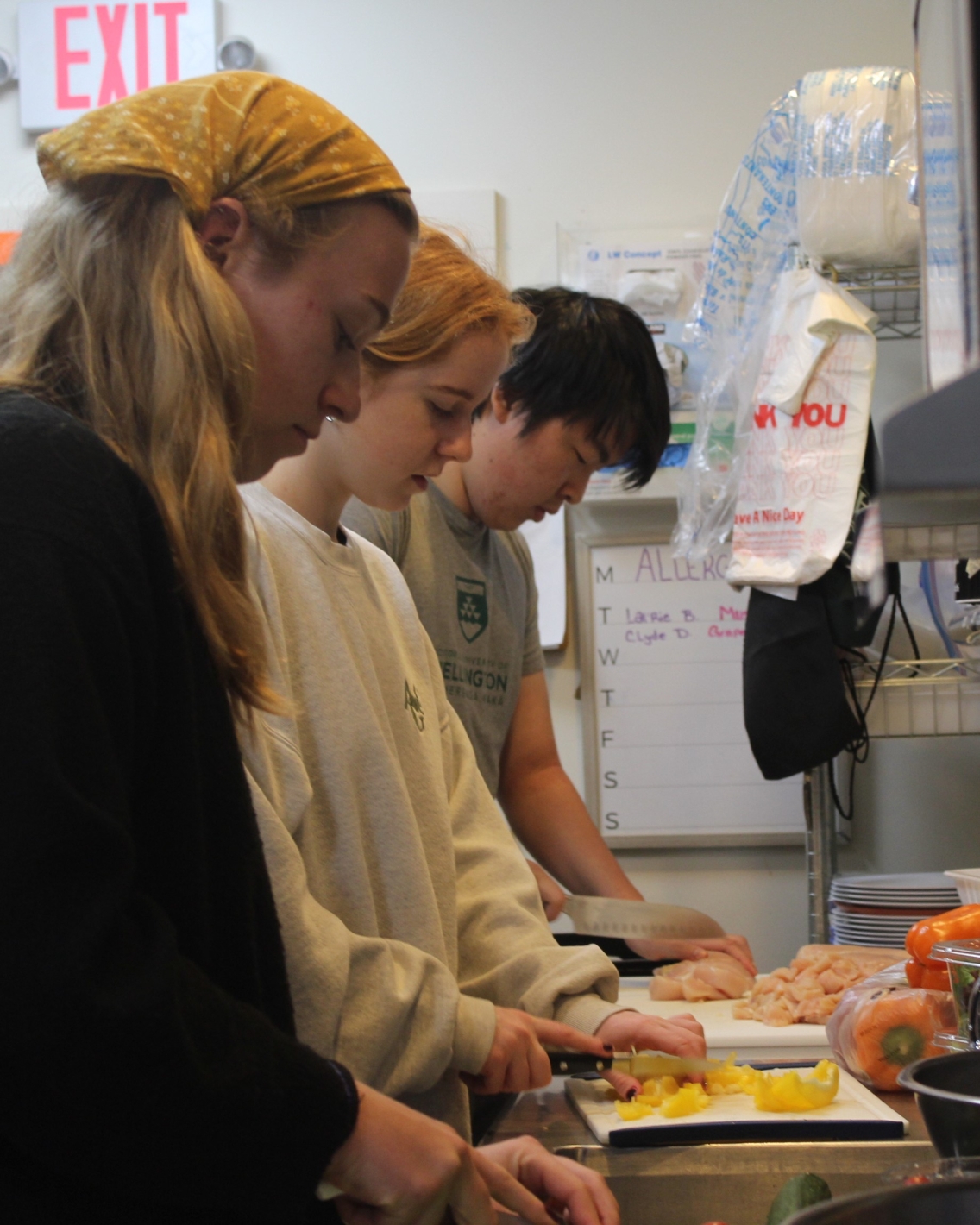 Three student volunteers chopping vegetables at a kitchen counter.