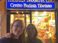 Two people posing in front of a bright window and blue sign