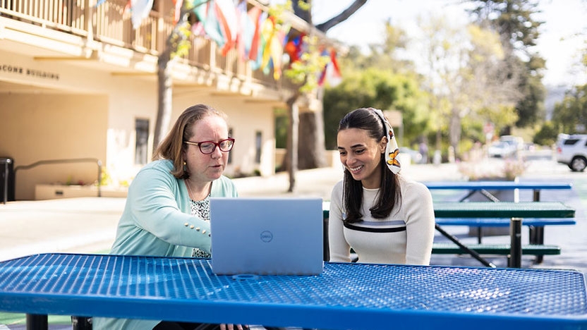 Netta and a student sitting outside on the MIIS campus and looking at a computer laptop together.