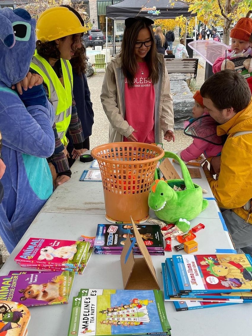 Page One volunteers in colorful costumes standing around table covered in children's books at a tabling event. 