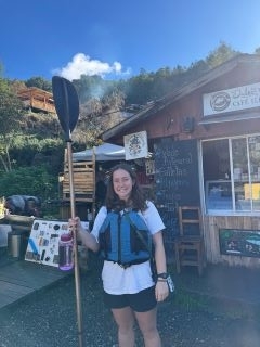 Student smiling while wearing a life jacket and holding a kayak paddle