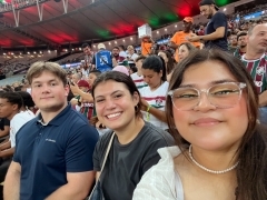Three students smiling in a crowded stadium