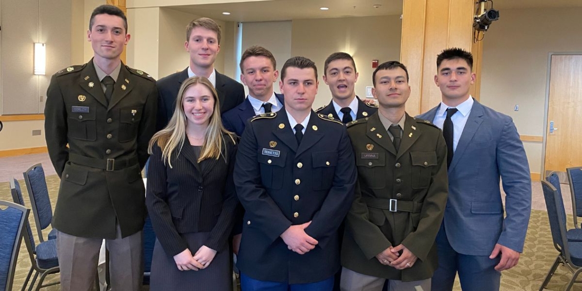 Group of ROTC students in uniform and suit and jacket smiling at the camera.
