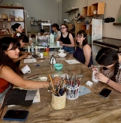 Group of students gathered around a table and painting pottery