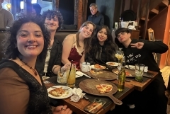 Five students smiling around a table with pizza