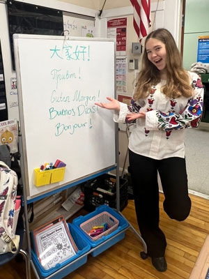 Student presenting "Good Morning" in several languages on a whiteboard.