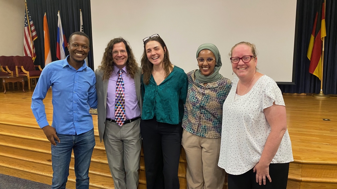 Two men and three women are smiling, their arms are around each other