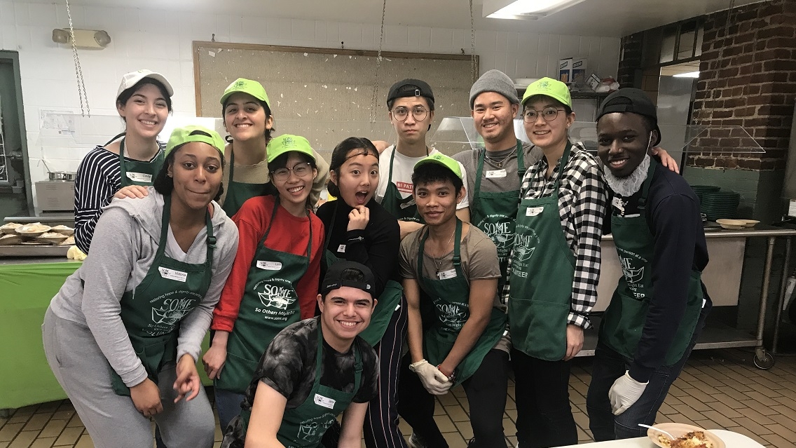 A group of students stand wearing matching green aprons and bright green hats, smiling at the camera.