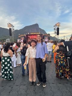 Two students posing in front of a music festival stage and mountain
