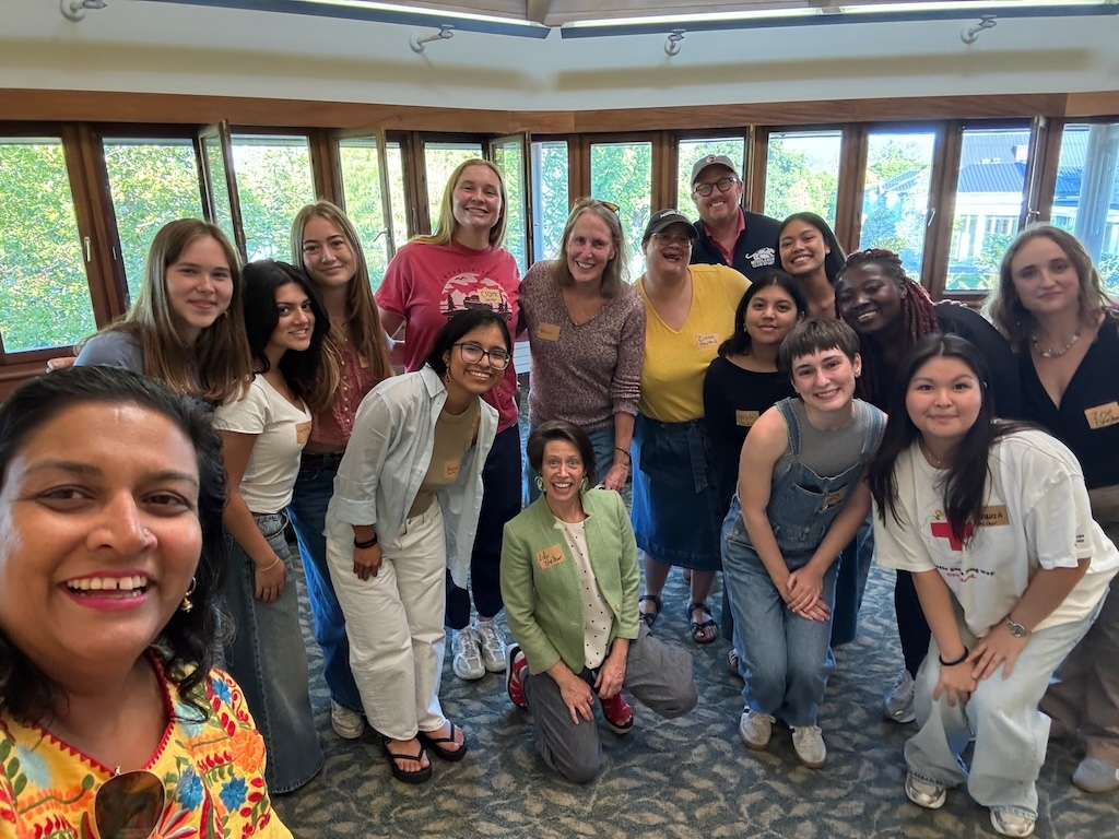 a group of young people take a selfie in a room lined with windows.