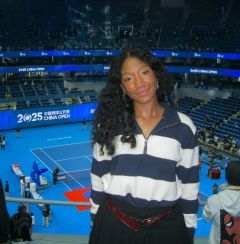 Student posing in front of a blue tennis stadium