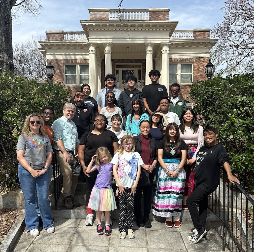 a large group of people stand on the steps of a large manor with white columns on the front of the house.
