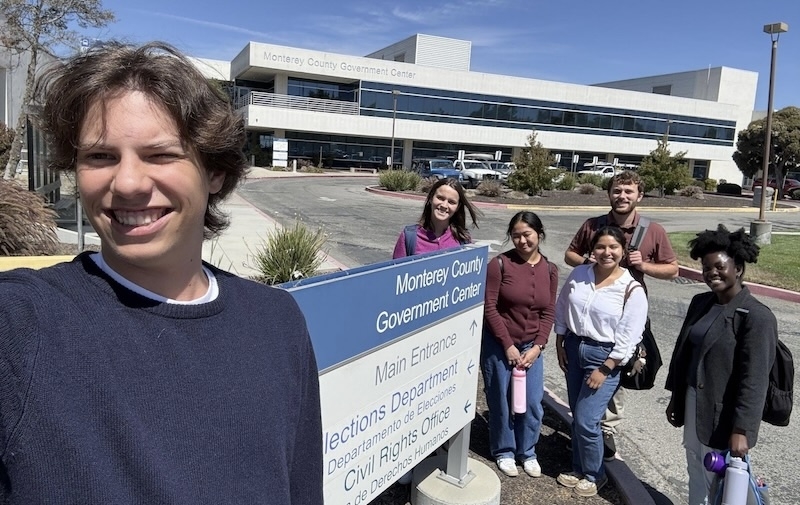 a young man takes a group selfie next to a large building sign for local Monterey California government