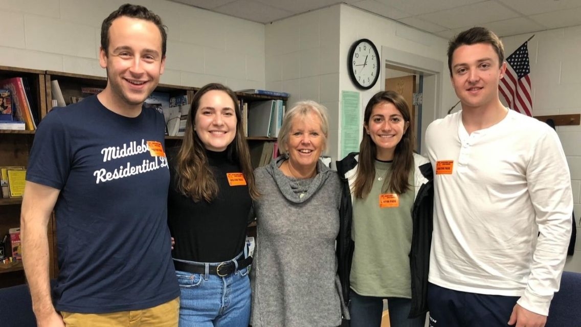 five people standing in a row pose for a photo in a classroom
