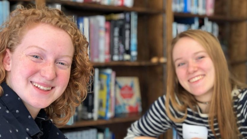 MiddCAM mentor and mentee smile for a photo against the backdrop of bookshelves
