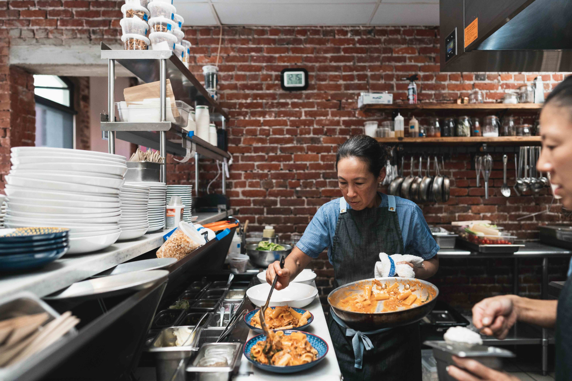 Robynne Maii works in the kitchen of her restaurant Fête, adding an orange sauce to a pasta dish.