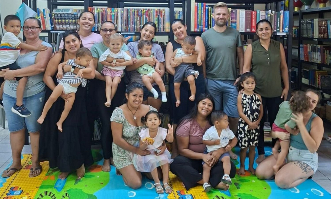 A group of people from the Nosara community gather in the library for a group photo. There are babies and toddlers and their families, as well as the Director.
