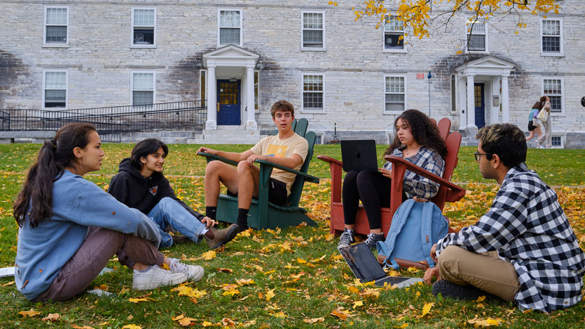 Students sit on the grass in a circle talking.