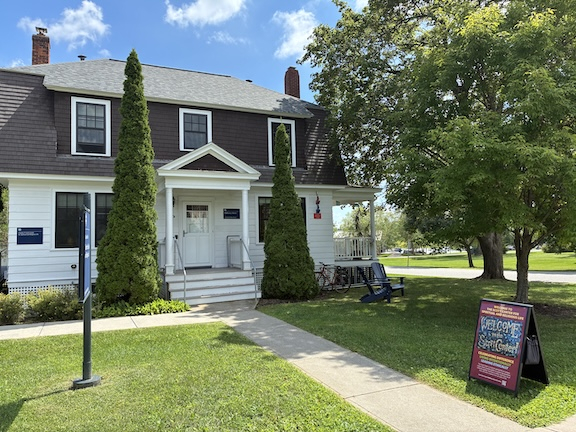two-story brown and white house with welcome sign and blue sky