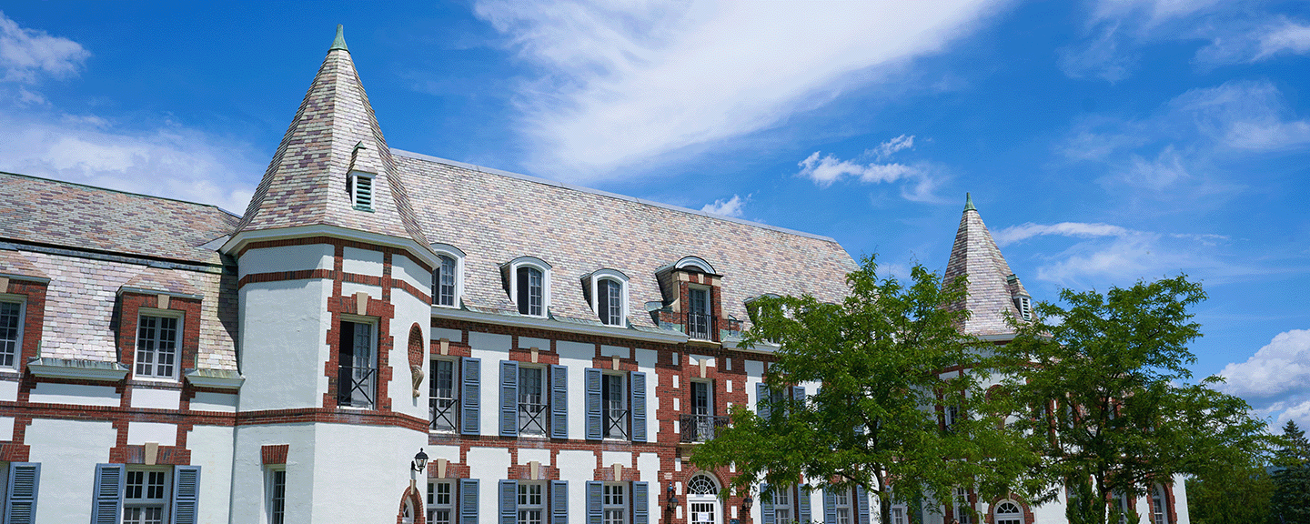 the Chateau's white walls and red bricks contrast against a blue summer sky with fluffy white clouds