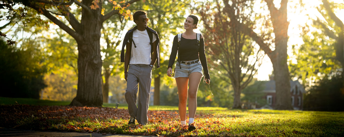 Two students walking side by side along a sunlit campus trail.