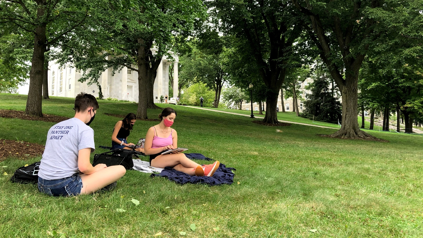 Three Middlebury students sit with masks on lawn and study.