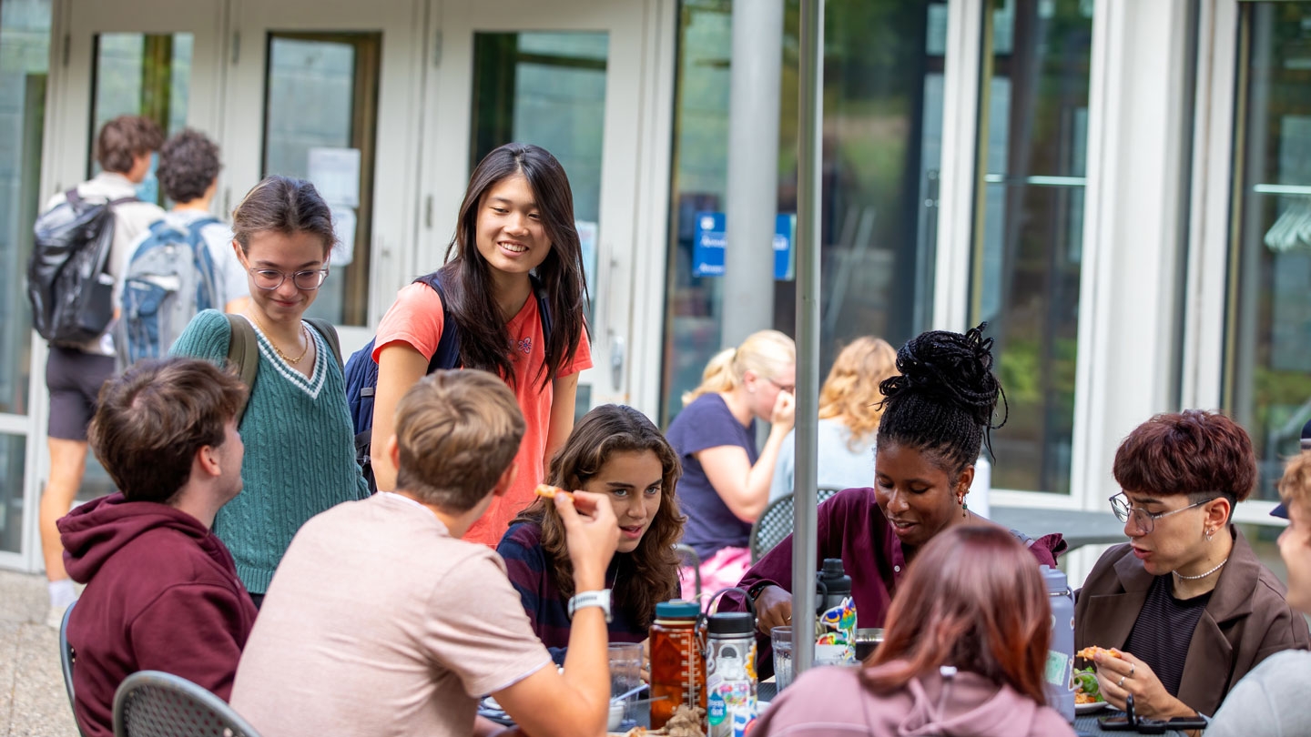 A group of students around a table outside a dining hall on campus.
