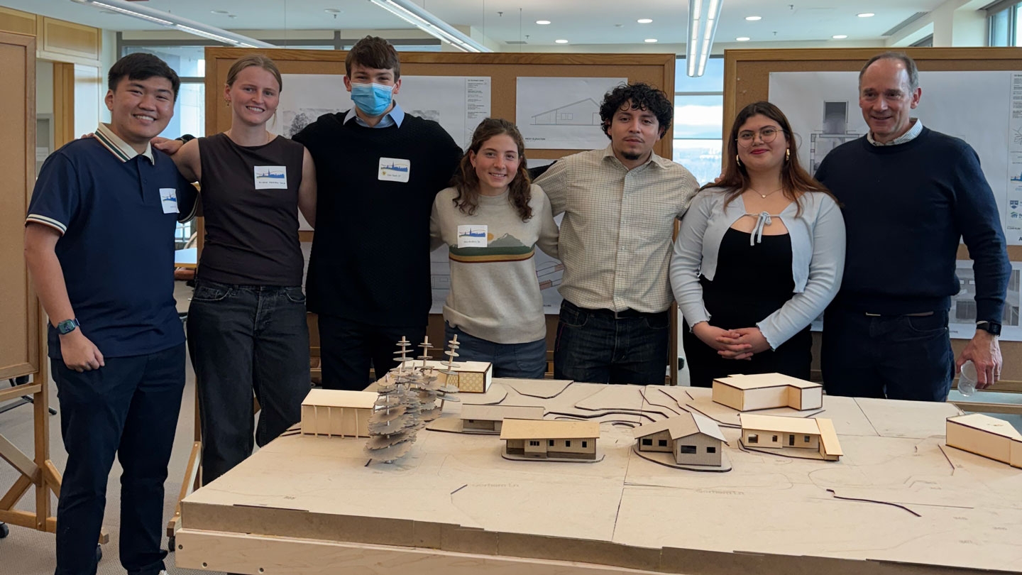 A group of students and faculty in front of an architectural model of local affordable homes.