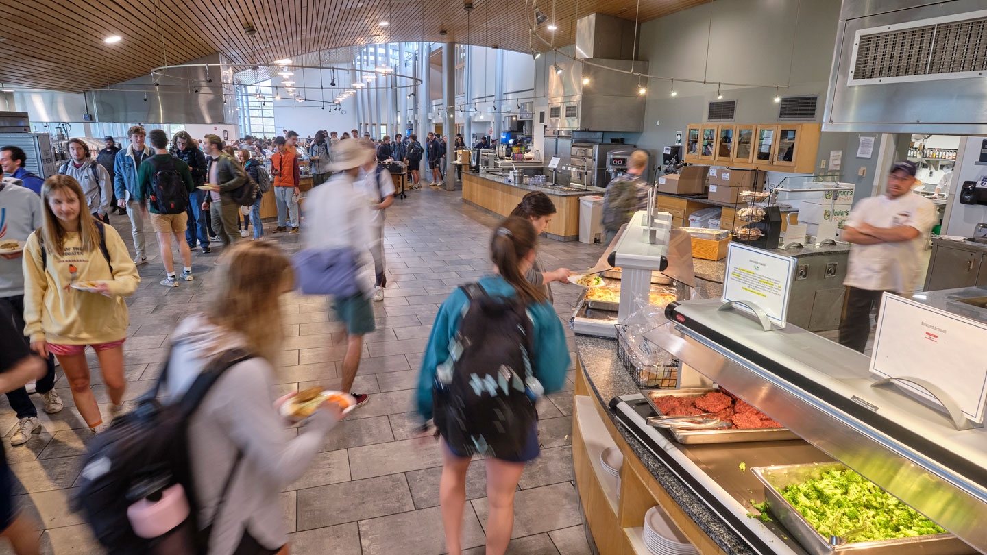 Students in a well lit dining hall with fresh food on trays.