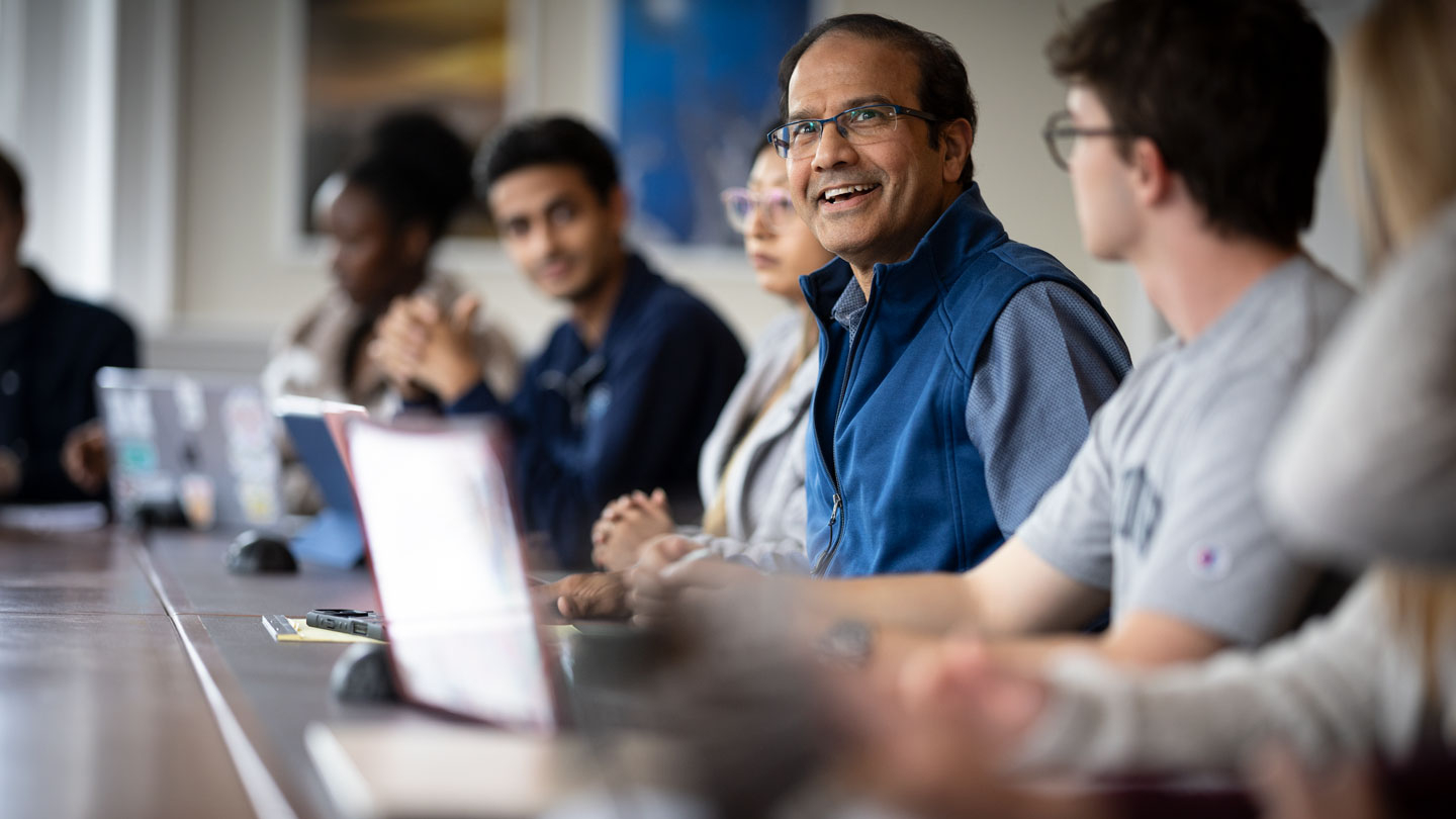 A Middlebury professor in the classroom at a table surrounded by students.