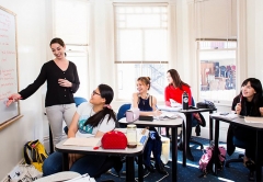 Teacher gesturing towards whiteboard while students look on smiling