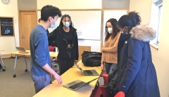 Four students in a classroom looking at laptops and discussing their project.