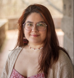 Alejandra Morales Torres, wearing a pink shirt and beige cardigan, poses for a photo in front of a brown, wooden, deck.