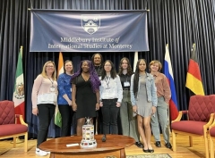 seven students and teachers in front of banner and between flags