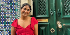 Narjis Nusaibah poses in a red dress in front of a green door and tiled wall.