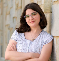 Addie leaning against a stone wall with arms crossed