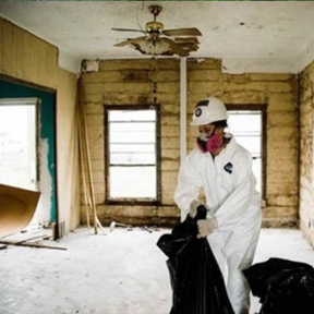 A person in white hazard gear cleaning up a damaged home