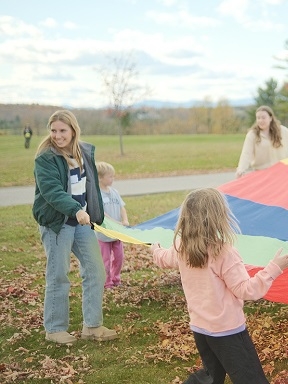 Two adults and two children stand and hold a large multicolored parachute.