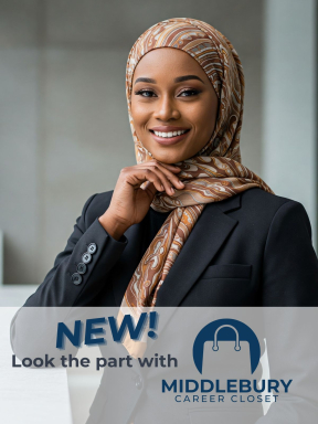 A young woman with a grey suit jacket and a brown patterened headscarf poses and smiles into the camera