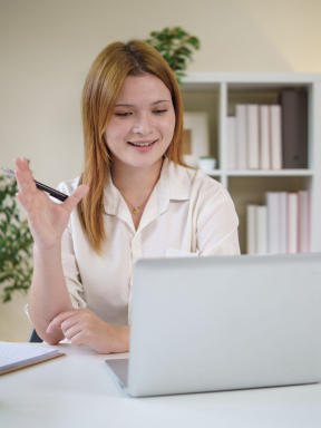 A young woman iwth long blond hair practices answering interview questions while looking into her laptop camera.