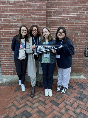 Four people stand side by side and smile at the camera, while holding a Middlebury flag.