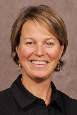 A woman with short, blonde hair and a black button-down shirt smiles into the camera.