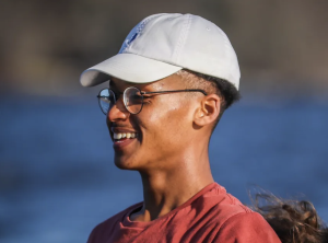 A man in a white cap and glasses wearing a red shirt is looking sideways and smiling.