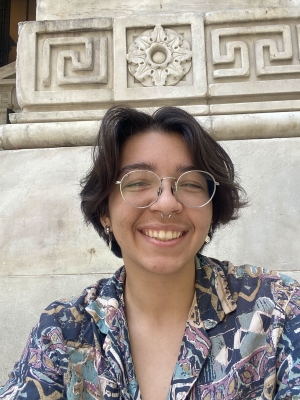 A person wearing round glasses and a patterned shirt is smiling.
