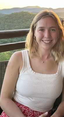 A person with blonde hair, white tank top and red skirt is smiling.
